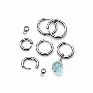 May include: A collection of silver-toned metal hoop earrings in various sizes, including several plain circular hoops with hinged closures, two small cylindrical jump rings, and one hoop earring featuring a dangling raw light blue crystal.