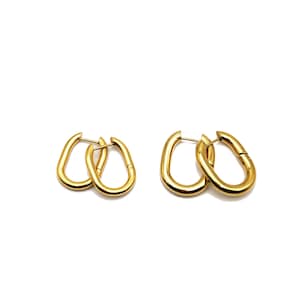 May include: A pair of gold oval hoop earrings. The earrings are made of a thick, smooth metal and have a simple, modern design.