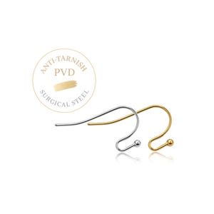 May include: Two earring hooks, one silver-toned and one gold-toned, featuring a curved wire design with a small ball at the end. A circular emblem above the hooks displays the text ANTI-TARNISH PVD SURGICAL STEEL with a gold brush stroke graphic.