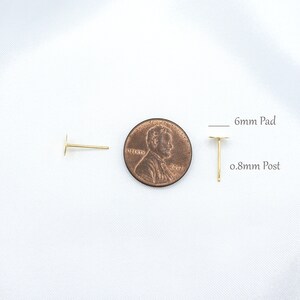 May include: Two gold-colored earring posts with flat circular pads. One post is shown from the side, and the other is shown upright next to a copper-colored penny. Text indicates a 6mm pad and a 0.8mm post for these jewelry components.