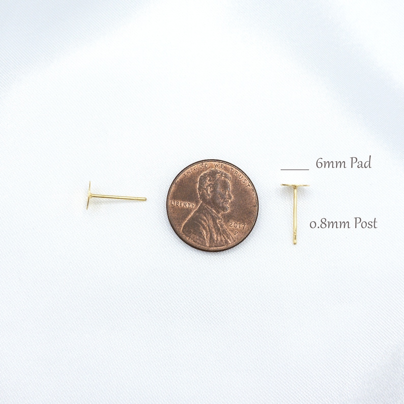 May include: Two gold-colored earring posts with flat circular pads. One post is shown from the side, and the other is shown upright next to a copper-colored penny. Text indicates a 6mm pad and a 0.8mm post for these jewelry components.