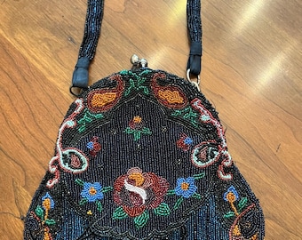 Puede incluir: Un bolso de noche vintage de cuentas con un diseño floral en tonos azules, rojos, verdes y naranjas. El bolso tiene una correa de cuentas negras y un cierre plateado.