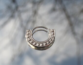 Könnte beinhalten: Silberner Septumring mit Perlenmuster. Der Ring ist offen und bereit zum Tragen.