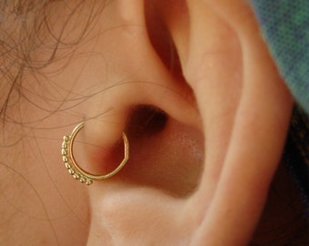 May include: A close-up of a person's ear with a gold hoop earring. The earring is made of small beads.