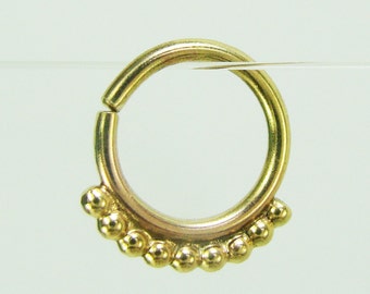 May include: Gold body jewelry with a beaded ring. The ring is made of a smooth, shiny metal and has a row of small, round beads around the bottom.