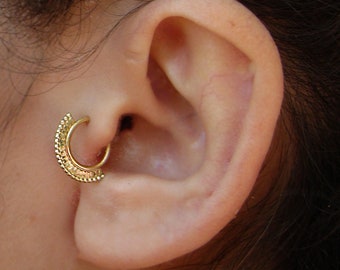 May include: A gold hoop earring with a decorative design. The earring is worn in the upper cartilage of the ear.