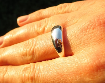 May include: A silver ring with a smooth, rounded, and polished surface. The ring is worn on a finger.