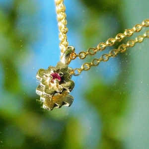 May include: A gold chain necklace with a small, intricate pendant featuring a red gemstone in the centre. The pendant is shaped like a flower with multiple layers of petals.