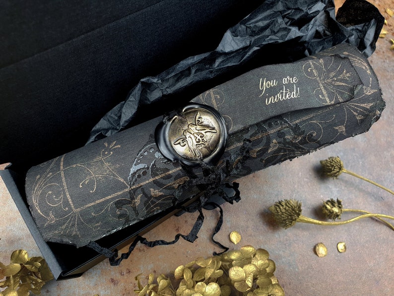 May include: A black scroll with gold accents and a wax seal. The scroll is rolled up and tied with a black ribbon. The text on the scroll reads "You are invited!"