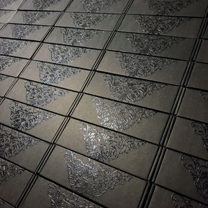 May include: A close-up view of a stack of black boxes with a silver embossed design. The boxes are arranged in a staggered pattern.
