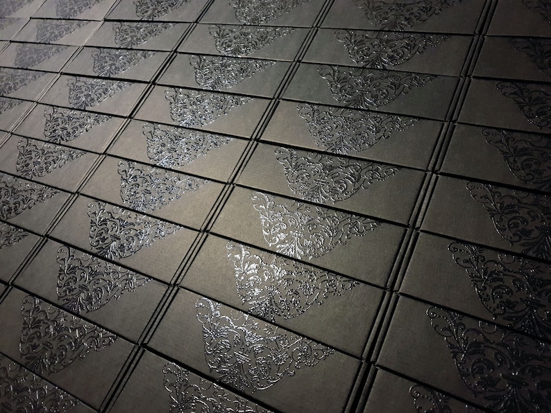 May include: A close-up view of a stack of black boxes with a silver embossed design. The boxes are arranged in a staggered pattern.