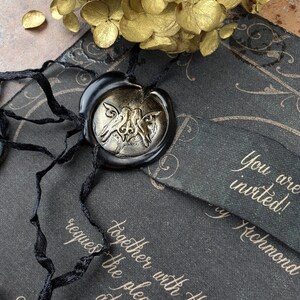 May include: A black and gold wedding invitation with a wax seal featuring a stylized bird design. The invitation reads "You are invited! By Richmond together with their family requests the pleasure of your presence at their wedding."