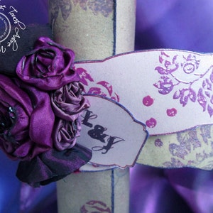 Puede incluir: Rosas de cinta de satén morado adornan un rollo decorativo con un diseño floral rosa y blanco y el texto "L & J".