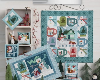 May include: A display of winter-themed quilted items, including wall hangings, pot holders, and a pillow. The designs feature snowmen, houses, trees, and mugs in shades of blue, green, and white. The text "Frost Hill On Wander Lane" and "Art to Heart" are visible.