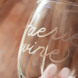 May include: A clear glass wine glass with the words "Fairy Wine" etched into the side.