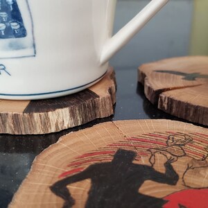 May include: A white ceramic mug with a blue typewriter design and the word "EWRITER" rests on a wooden coaster. Additional wooden coasters with painted designs of birds and a figure are also visible.