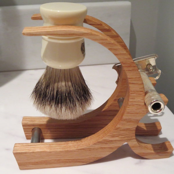 May include: A wooden stand with a white shaving brush and a silver safety razor. The stand is made of light brown wood and has a curved design.