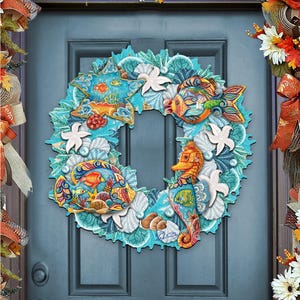 May include: A decorative wreath featuring a sea life theme, with colorful fish, seahorses, starfish, and seashells. The wreath is predominantly turquoise and white, with accents of orange, yellow, and blue. It is displayed on a blue door, with fall foliage accents.