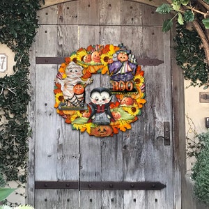 Peut inclure: Une couronne d'Halloween aux couleurs jaune, orange et marron. La couronne repr&eacute;sente une momie, un vampire, une sorci&egrave;re et des citrouilles. La couronne porte &eacute;galement le mot "BOO".