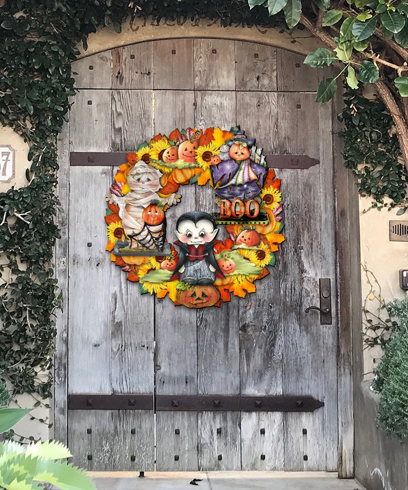 Peut inclure: Une couronne d'Halloween aux couleurs jaune, orange et marron. La couronne repr&eacute;sente une momie, un vampire, une sorci&egrave;re et des citrouilles. La couronne porte &eacute;galement le mot "BOO".