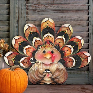 May include: A decorative turkey cutout featuring a large, fan-shaped tail with black and orange leaf-patterned feathers. The turkey has a light brown body, a yellow beak, a red wattle, and holds a small chick wearing a black top hat.