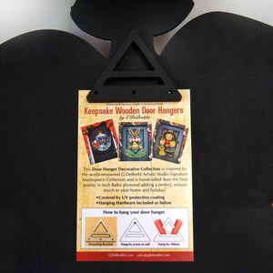 May include: A white card with a black border and text that reads "Keepsake Wooden Door Hangers by G.DeBrekht". The card shows three images of wooden door hangers with different holiday themes. The text also includes instructions on how to hang the door hangers.