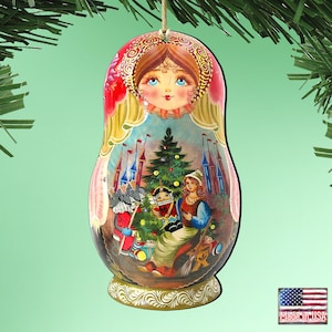 May include: A hand-painted wooden ornament in the shape of a Matryoshka doll. The ornament features a woman's face at the top and a scene with a Christmas tree, a castle, and figures from a fairy tale. The ornament is suspended by a string.