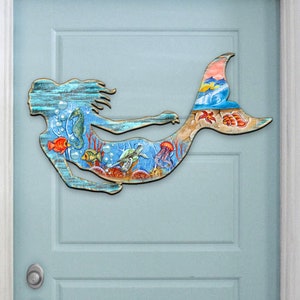 May include: A wooden mermaid wall decor with a blue, green, and orange painted design. The mermaid is surrounded by sea life, including fish, sea turtles, and a seahorse.