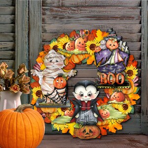 Peut inclure: Une couronne d'Halloween avec une vari&eacute;t&eacute; de couleurs d'automne, y compris l'orange, le jaune et le brun. La couronne repr&eacute;sente une momie, un vampire et un &eacute;pouvantail, ainsi que des citrouilles, des tournesols et des feuilles. La couronne porte &eacute;galement le mot "BOO".