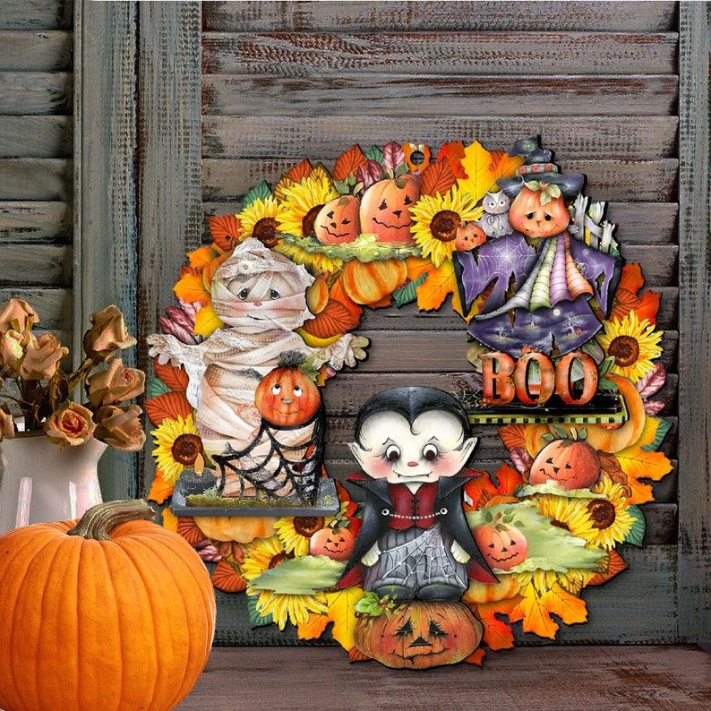 Peut inclure: Une couronne d'Halloween avec une vari&eacute;t&eacute; de couleurs d'automne, y compris l'orange, le jaune et le brun. La couronne repr&eacute;sente une momie, un vampire et un &eacute;pouvantail, ainsi que des citrouilles, des tournesols et des feuilles. La couronne porte &eacute;galement le mot "BOO".