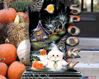 May include: A decorative wooden sign shaped like a tombstone with the word SPOOKY vertically on the right side. The illustration features a purple house, a full moon, bare trees, spiderwebs, and a cartoon ghost holding a small orange pumpkin.
