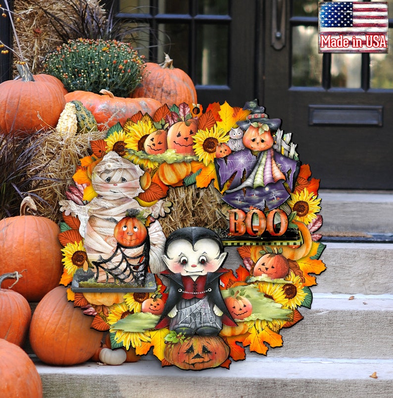 Peut inclure: Une couronne d'Halloween avec des personnages de momie, de vampire et de sorci&egrave;re. La couronne est d&eacute;cor&eacute;e de tournesols, de citrouilles et de feuilles d'automne. Le texte "BOO" est affich&eacute; sur la couronne.