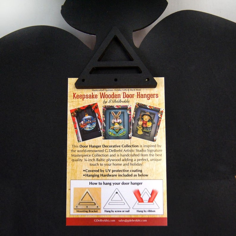Może przedstawiać: Biała karta z czarną ramką i nadrukowanym tekstem "Keepsake Wooden Door Hangers by G.DeBrekht". Karta przedstawia trzy r&oacute;żne wieszaki na drzwi z motywami świątecznymi. Karta zawiera r&oacute;wnież instrukcje dotyczące sposobu zawieszania wieszak&oacute;w na drzwiach.