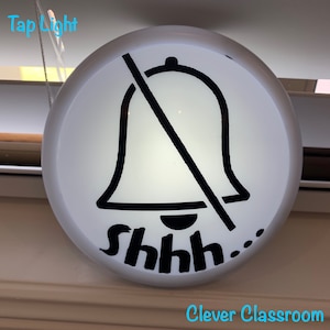 May include: A white round sign with a black bell crossed out and the text "shhh..."  The sign is hanging from a white string. The text "Clever Classroom" is printed in blue below the sign.