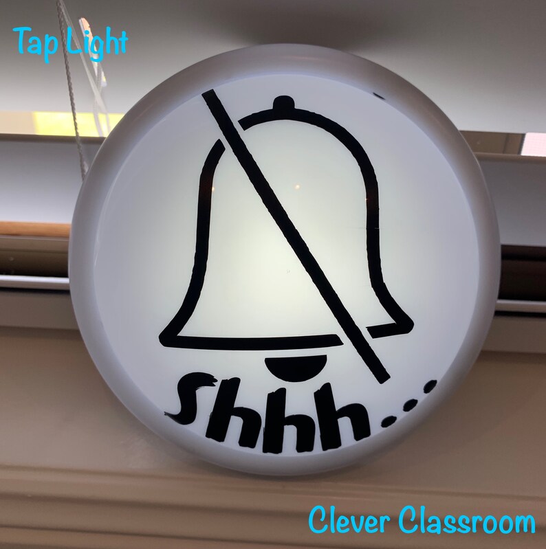 May include: A white round sign with a black bell crossed out and the text "shhh..."  The sign is hanging from a white string. The text "Clever Classroom" is printed in blue below the sign.