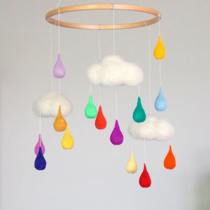 May include: A colourful felt baby mobile with a wooden ring, two white clouds, and rainbow-coloured raindrops hanging from it.