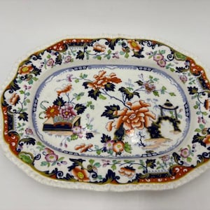 May include: Oval ceramic serving platter with a scalloped edge. The platter features a floral design with orange, pink, and blue flowers, and a blue border. The rim has a red and green pattern.