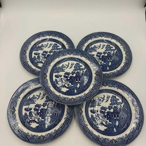 May include: A set of five round ceramic plates featuring a blue and white willow pattern. Each plate displays a detailed transferware scene of pagodas, trees, birds, and a bridge, framed by a decorative geometric border along the outer rim.