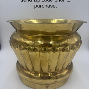May include: A polished brass planter featuring a wide, flared rim and a rounded body with vertical fluted detailing. The surface has a metallic gold finish with subtle variations in texture and tone across the exterior of the vessel.