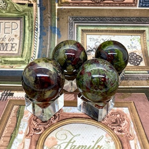 May include: Four green, red and black patterned spheres on clear stands. The spheres are made of polished stone and have a smooth, glossy finish.