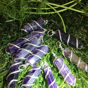 May include: A collection of seven amethyst crystal pendants wrapped in silver wire. The pendants are displayed on a green artificial grass surface.