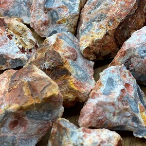 Puede incluir: Una colección de piedras naturales, sin pulir, multicolores con tonos de rojo, blanco, marrón y gris. Las piedras tienen un aspecto moteado y en capas.