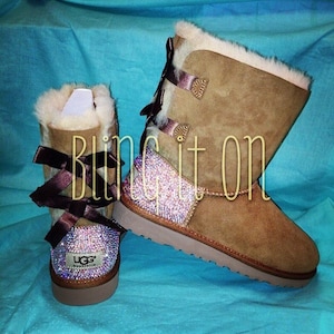 May include: A pair of brown suede boots with a decorative bow and rhinestones. The boots are decorated with the text "Bling it on".