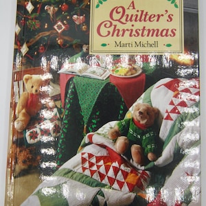 May include: A Rodale Quilt Book titled "A Quilter's Christmas" by Marti Michell. The book cover features a festive scene with a Christmas tree, teddy bears, and a quilt. The quilt has red, green, and white geometric patterns.