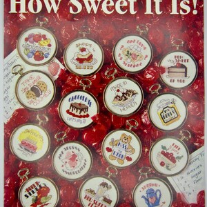 May include: A collection of 15 cross-stitch patterns for magnets, each featuring a sweet treat or dessert-themed design. The patterns are displayed in round frames against a red background with a cherry pattern. The title of the collection is "How Sweet It Is!" and the leaflet number is 2541.