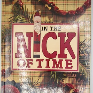May include: A book cover with a red plaid background and a green pine branch. The title of the book is "In the Nick of Time" in white letters on a red background. A cartoon Santa Claus is on the cover.