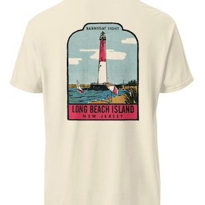 Könnte beinhalten: Ein cremefarbenes Kurzarm-T-Shirt mit einem Grafikdruck auf der Rückseite. Die Abbildung zeigt den Leuchtturm Barnegat Light, ein Segelboot und einen Sonnenschirm. Der Text lautet BARNEGAT LIGHT, LONG BEACH ISLAND und NEW JERSEY.