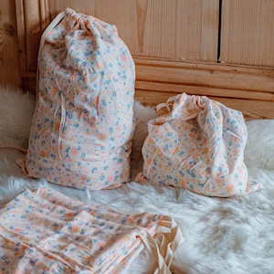 Peut inclure: Trois sacs à cordon avec un imprimé floral dans des tons de rose, bleu et jaune. Les sacs sont faits d'un tissu doux et léger, idéal pour ranger de petits objets.