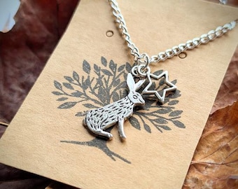 May include: A silver necklace with a charm of a rabbit and a star. The necklace is on a brown card with a tree design.