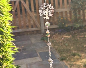 May include: A hanging suncatcher ornament featuring a silver-toned metal tree of life charm, a small sun charm, and several clear faceted glass crystals. The decorative piece is strung on a thin silver chain with small peach and green stone beads.